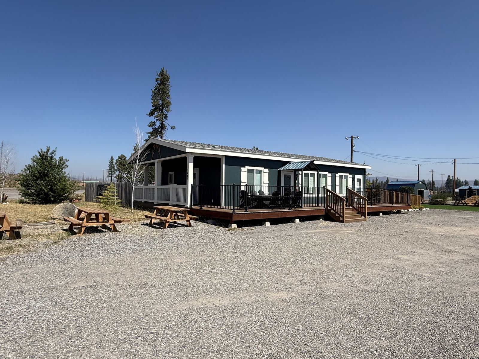 The three bedroom house at Cedar Lodge with its covered porch, picnic tables and a tall pine behind it.