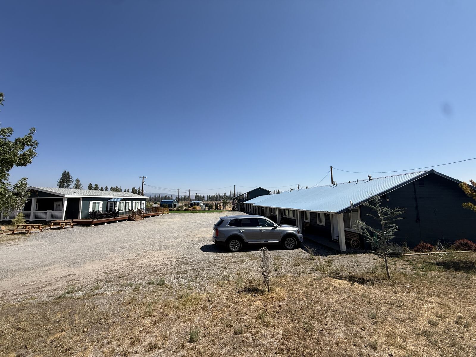 The whole of Cedar Lodge from the entrance: the house and its deck on the left, the motel row under a metal roof on the right, gravel parking between them.